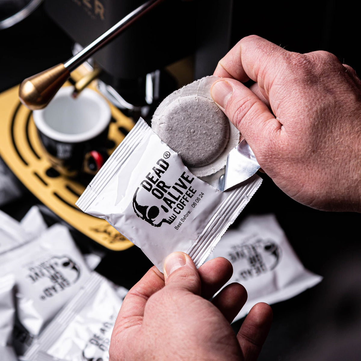 Hände öffnen ein DEAD OR ALIVE COFFEE ESE Pad an einer Espressomaschine