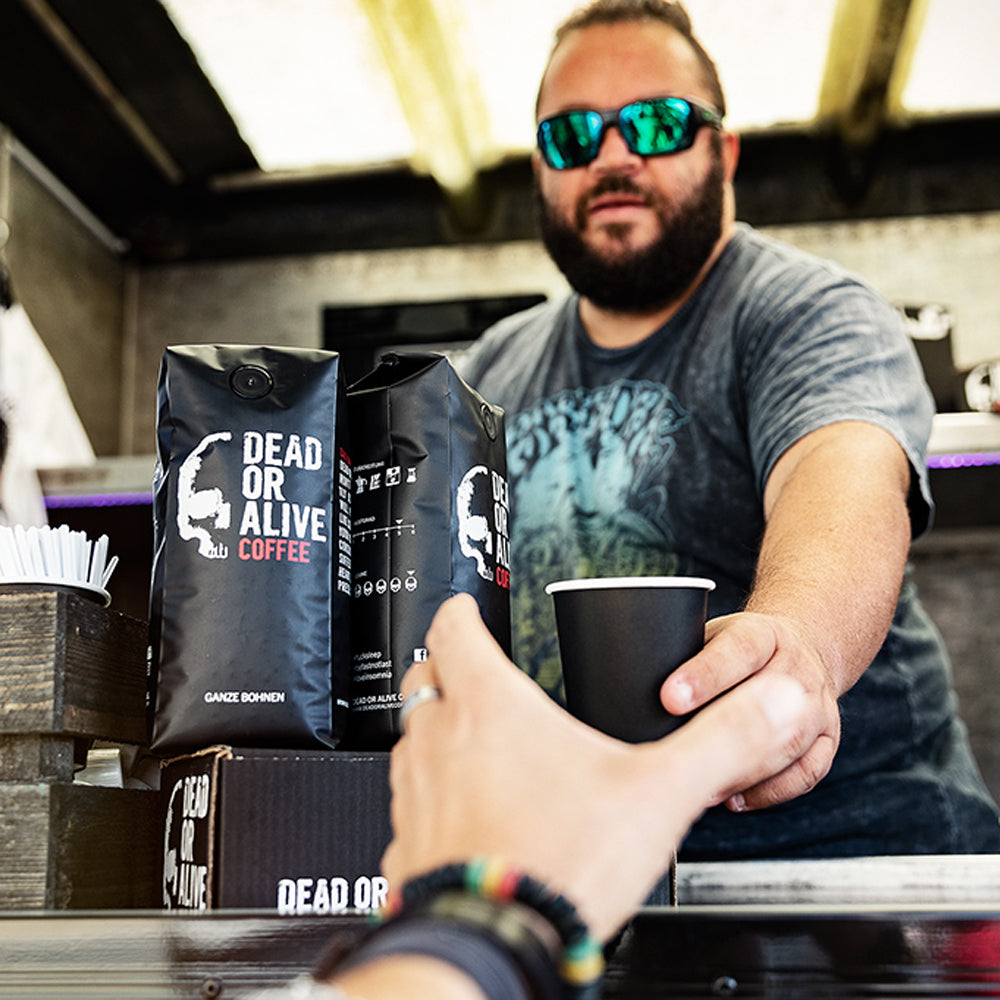 Mann serviert DEAD OR ALIVE COFFEE über einen Tresen