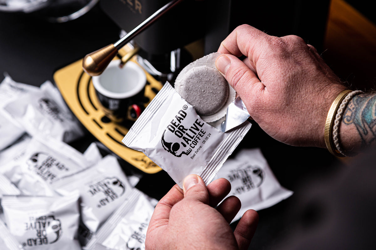 Hände öffnen ein DEAD OR ALIVE COFFEE ESE Pad vor einer Espressomaschine