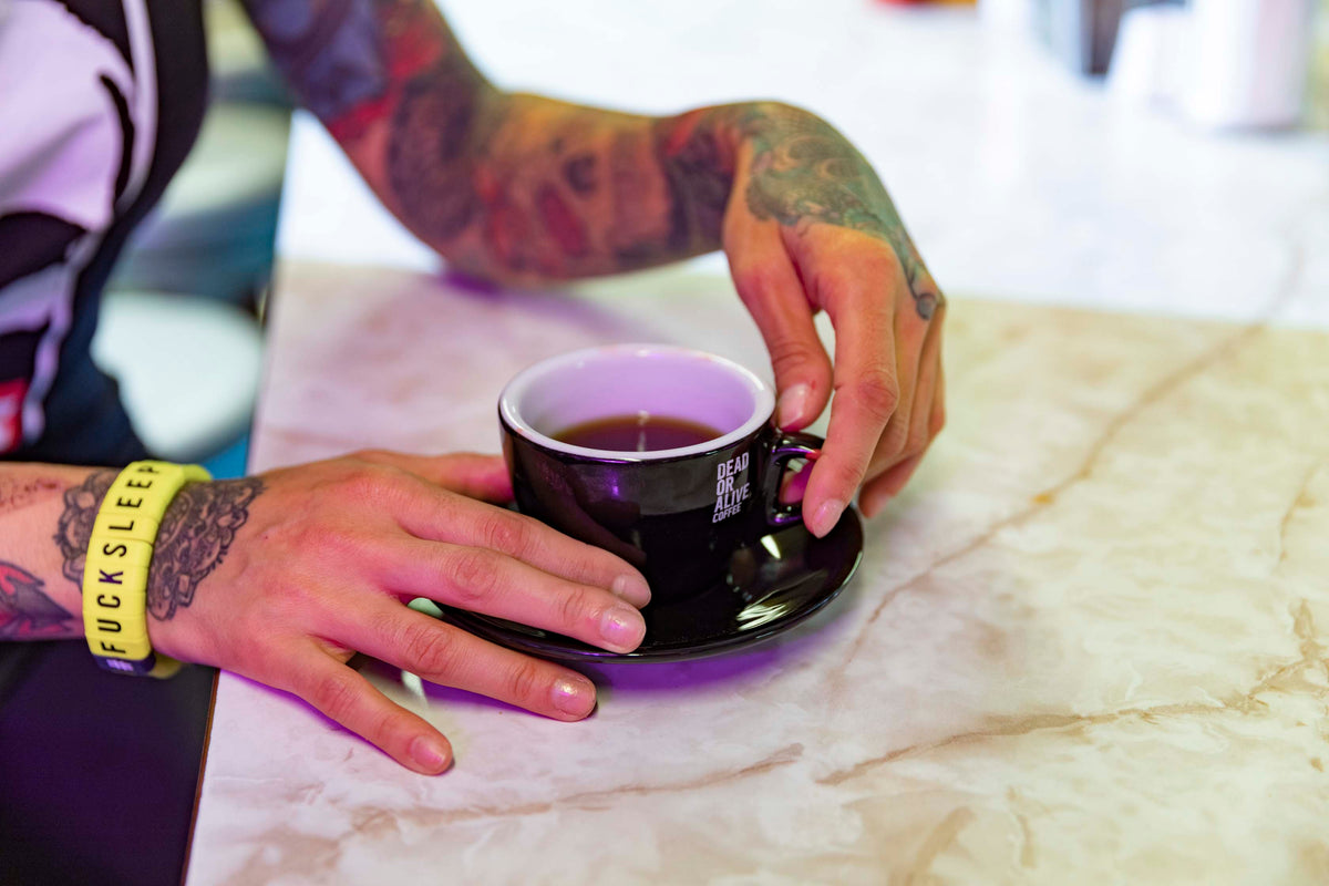 Tätowierte Hände halten eine schwarze Espressotasse