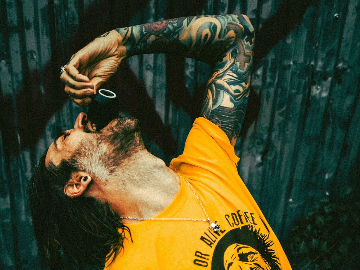 Mann im DEAD OR ALIVE COFFEE T-Shirt trinkt starken Espresso aus schwarzer Tasse