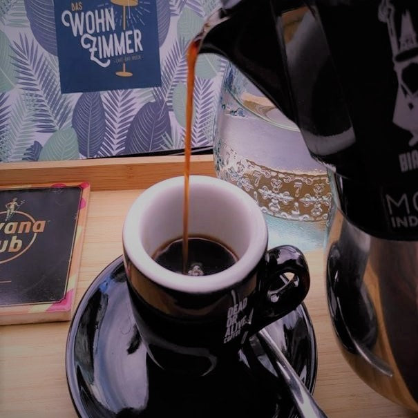 Kaffee aus der Espressokanne wird in eine schwarze DEAD OR ALIVE COFFEE Tasse gegossen